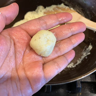 stretched hand showing a roll round dough ball which is white in color