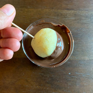 ball of dough being dipped into melted chocolate