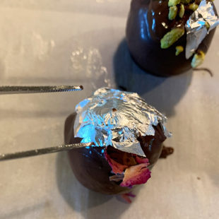 chocolate dipped round balls being decorated with edible silver leaves