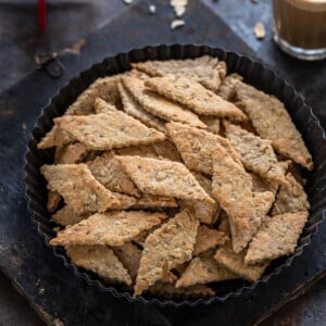 diamond shaped oats namak pare placed in a round plate with glass of chai in the background