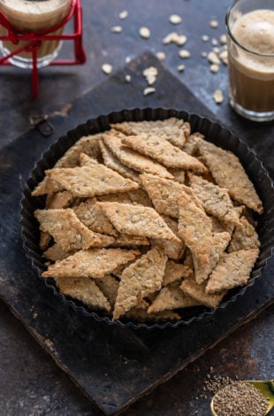 diamond shaped oats namak pare placed in a round plate with glass of chai in the background