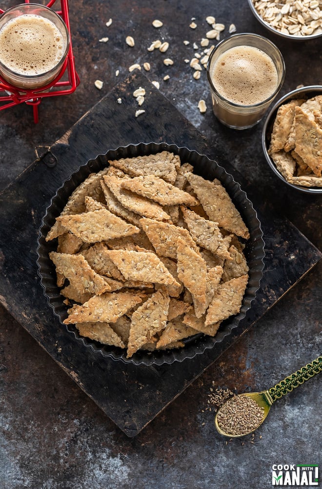 diamond shaped oats namak pare placed in a round plate with two glasses of chai in the background