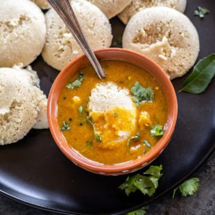 bowl of sambar with idli dipped into it and more idlis placed on the plate