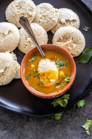 bowl of sambar with idli dipped into it and more idlis placed on the plate