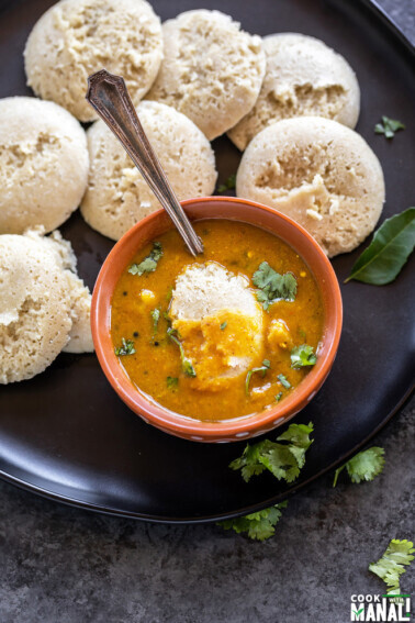 bowl of sambar with idli dipped into it and more idlis placed on the plate