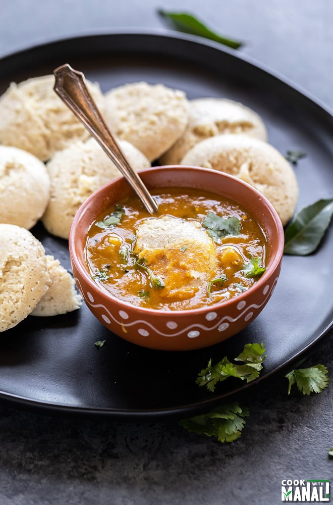 broken idli dunked in a bowl of sambar with more idlis in the background