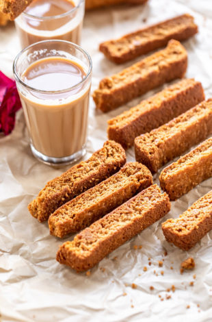 some rusk arranged on a tray with chai glasses in the background