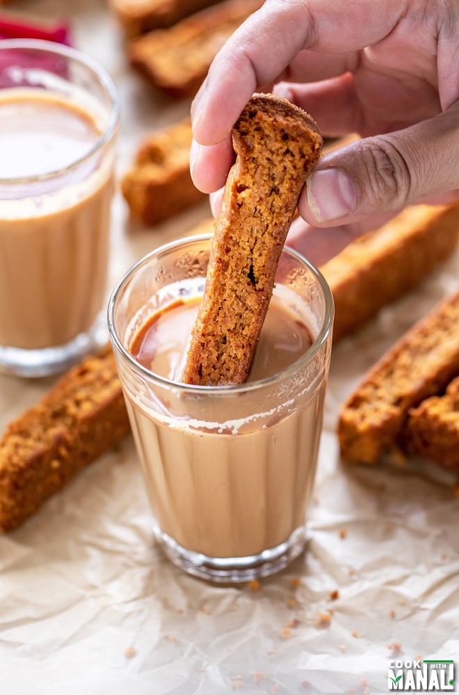 a hand dipping rusk in a glass of chai