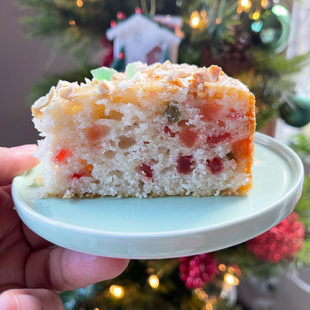 a hand holding a plate with a slice of cake with Christmas tree in backdrop