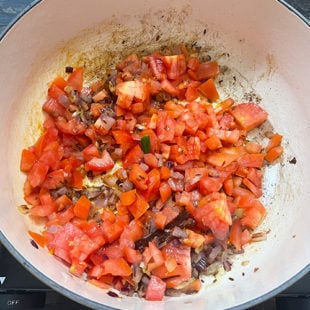 chopped tomatoes added to a pot with spices, onions