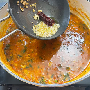 a small pan pouring over the tadka into a large pot