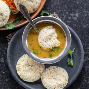 3 dal idli in a plate with 1 dipped in bowl of sambar