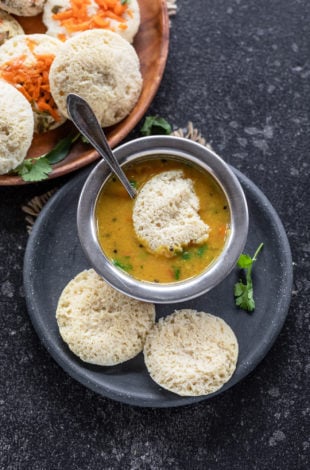 3 dal idli in a plate with 1 dipped in bowl of sambar