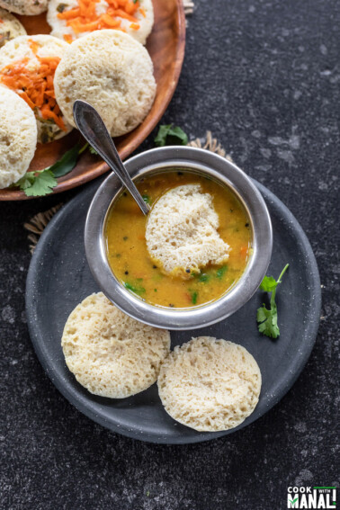 3 dal idli in a plate with 1 dipped in bowl of sambar