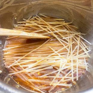 noodles being added to a pot with a spatula pressing them down
