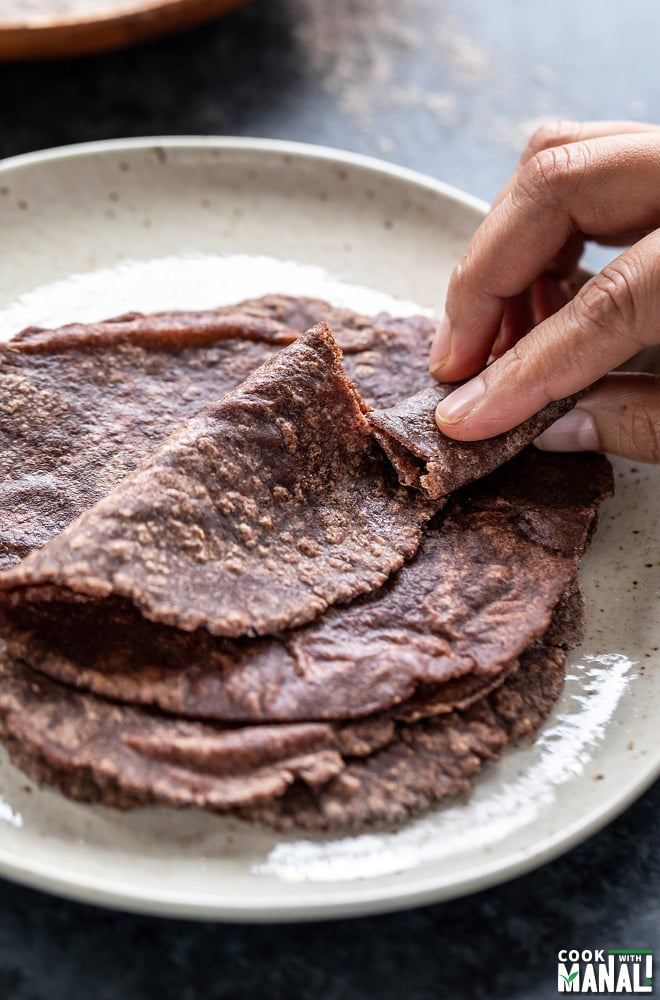 a hand breaking off a portion of the ragi roti