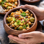 pair of hand holding a bowl of chickpea salad served in a wooden bowl