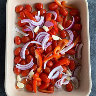 baking dish with cherry tomatoes, sliced onions, red peppers