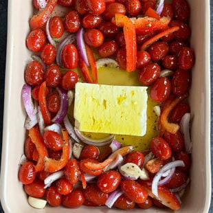 block of feta cheese placed in the center of a baking dish surrounded by cherry tomatoes