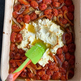 spatula mashing a block of feta cheese placed in a baking dish