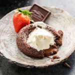 eggless chocolate lava cake served on a plate topped with ice cream and a strawberry and chocolate piece placed on the side