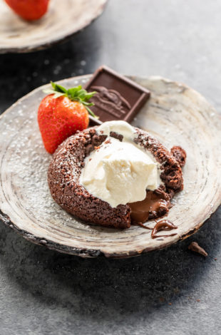 eggless chocolate lava cake served on a plate topped with ice cream and a strawberry and chocolate piece placed on the side