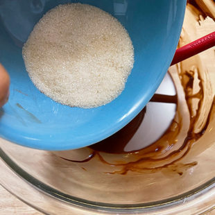 sugar being added to a bowl of melted chocolate and oil