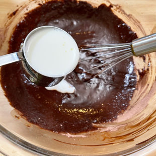 milk being added to a chocolate cake batter in a bowl