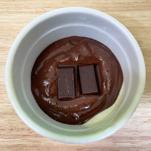 chocolate cake batter placed in a ramekin with chocolate pieces placed in the center