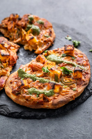 Naan Pizza placed on a black round board and drizzled with chutney