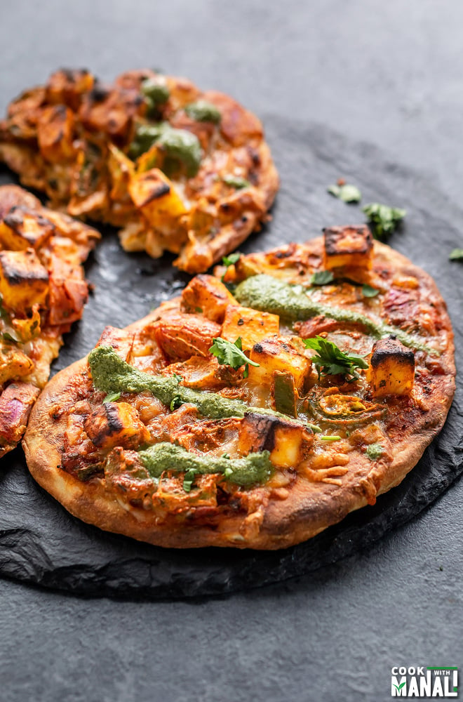 Naan Pizza placed on a black round board and drizzled with chutney
