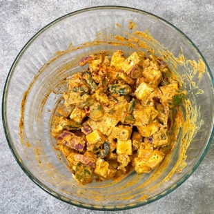 paneer, onion and peppers coated with a marinade in a bowl