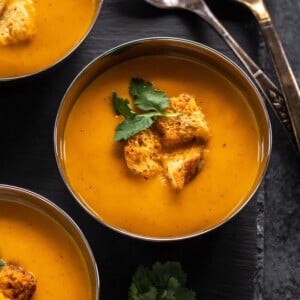 bowls of tomato soup topped with croutons and cilantro