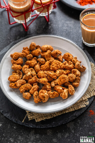 spice coated cashews on a plate with glass of chai on the side and also in the back