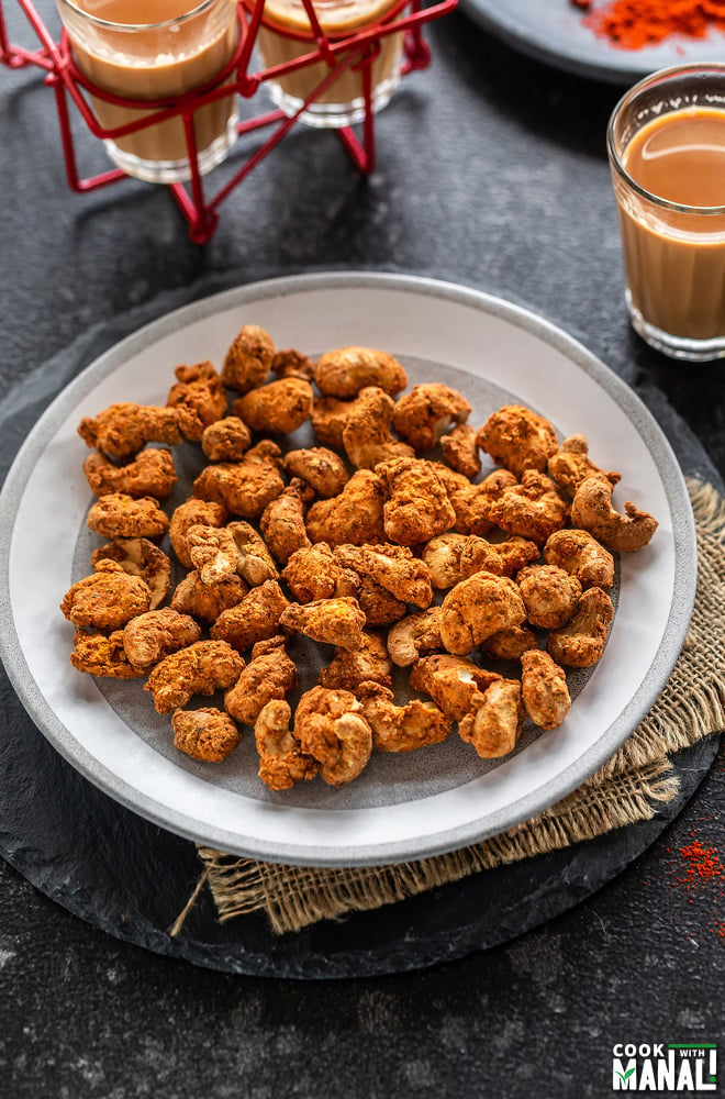 spice coated cashews on a plate with glass of chai on the side and also in the back