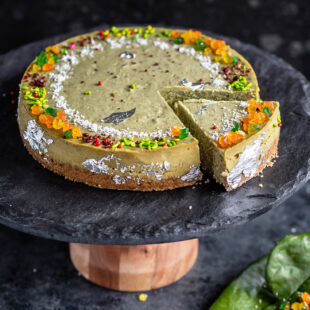 paan cheesecake served on a black stand with one piece cut from the cheesecake and few paan leaves on the side