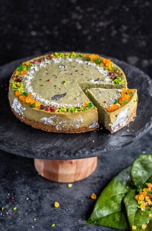 paan cheesecake served on a black stand with one piece cut from the cheesecake and few paan leaves on the side