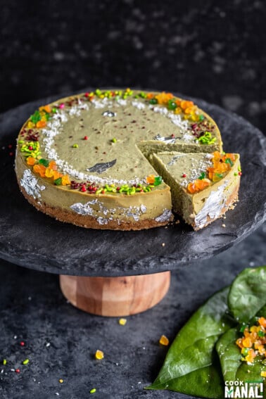 paan cheesecake served on a black stand with one piece cut from the cheesecake and few paan leaves on the side