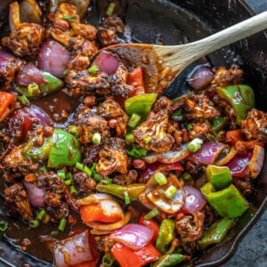 cast iron skillet with cauliflower, onions and peppers tossed in a sauce