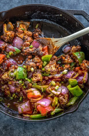 cast iron skillet with cauliflower, onions and peppers tossed in a sauce