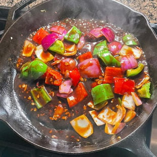 onions, peppers tossed in a sauce in a skillet