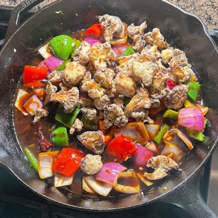 air fried cauliflower being added to a skillet with onions, pepper and sauce