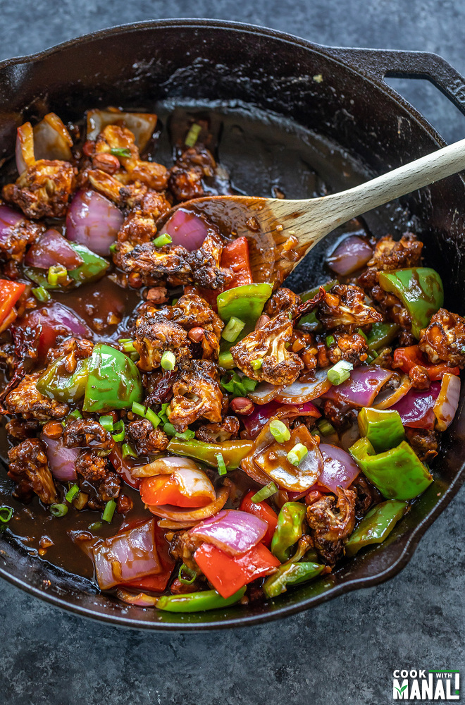 cast iron skillet with cauliflower, onions and peppers tossed in a sauce