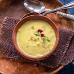 bowl with yellow color milk topped with rose petals and pistachios