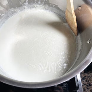 spatula scraping the sides of a pot filled with milk