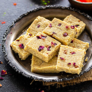 plate of thandai burfi with holi colors in the background