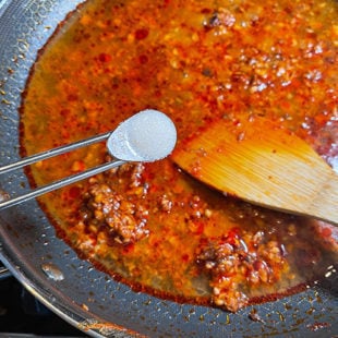 sugar being added to a pan with chili sauce