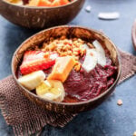 a coconut bowl filled with acai smoothie and topped with fruits, granola