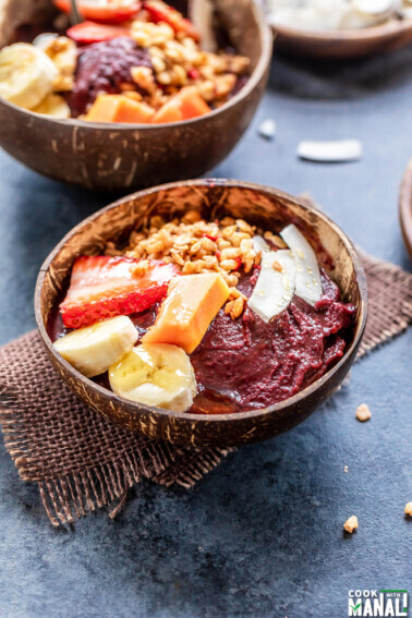 a coconut bowl filled with acai smoothie and topped with fruits, granola