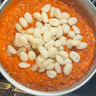 potato gnocchi being added to a pan of tomato sauce